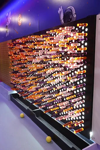 Interactive wall game with illuminated pegs in vibrant orange and white hues at an indoor kids trampoline park