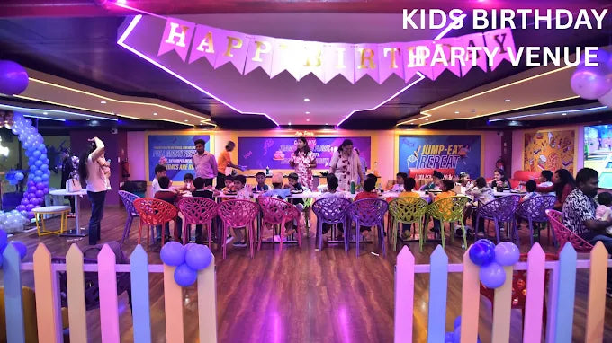 Children celebrating a birthday party in a colorful indoor play area with themed decorations and purple balloons