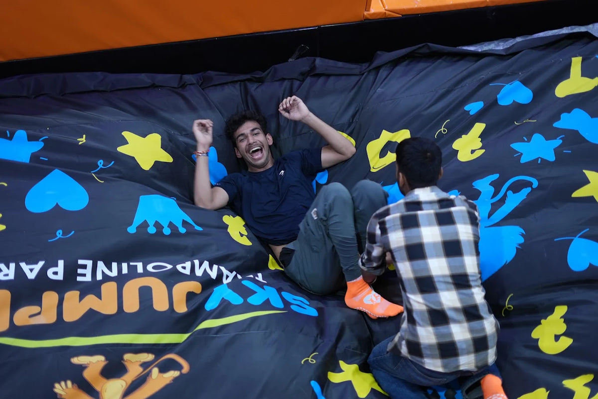 Two young men are having fun on a large inflatable surface with colorful graphics at a trampoline park.