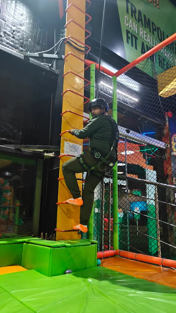 A person in a harness climbs a ladder at an indoor adventure park.