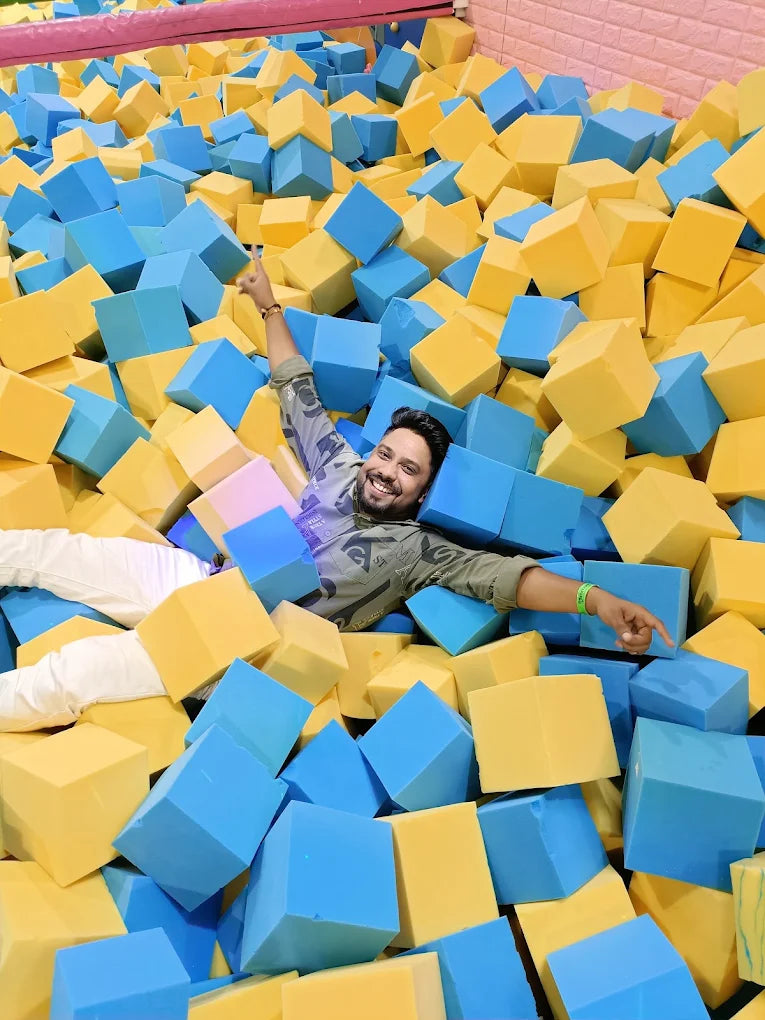 A man smiles while lying in a foam pit filled with blue and yellow cubes.