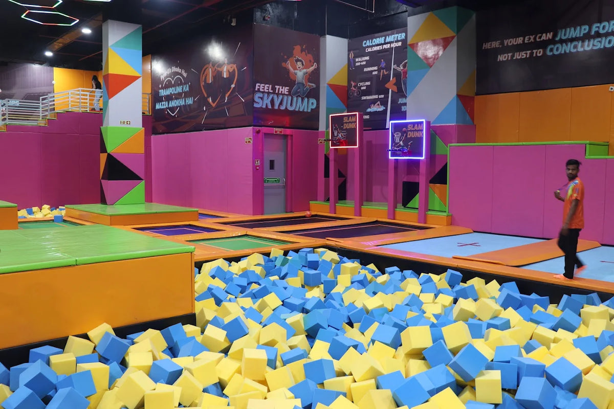 A trampoline park with a foam pit, featuring colorful padding and a young man walking.