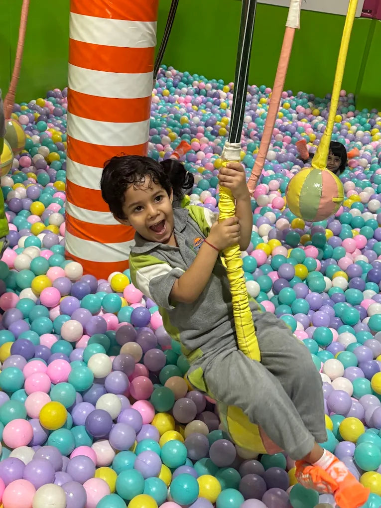 A young child swings joyfully in a ball pit filled with colorful balls.