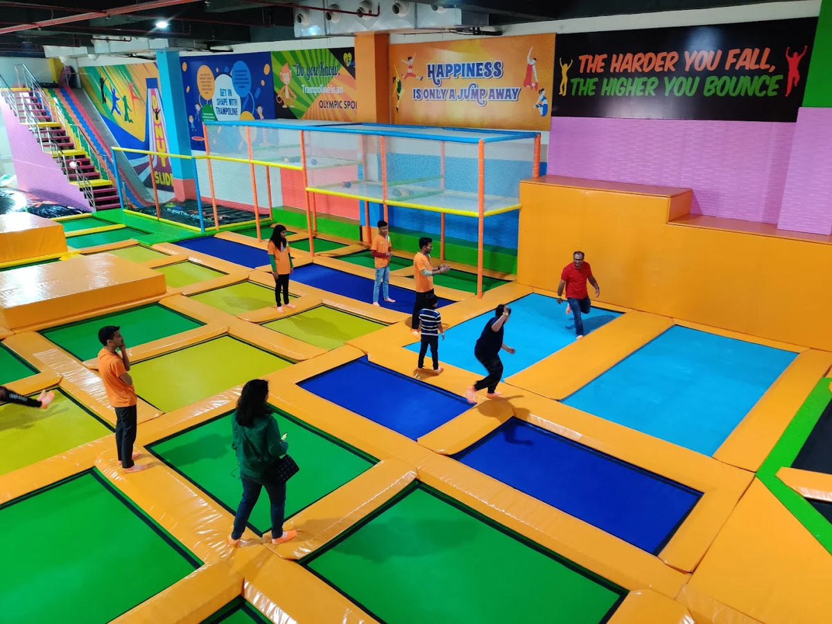 Young people jump on trampolines in a colorful indoor park.