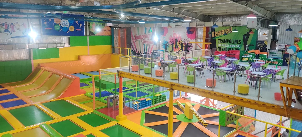An indoor trampoline park with colorful trampolines, seating areas, and a cafe.