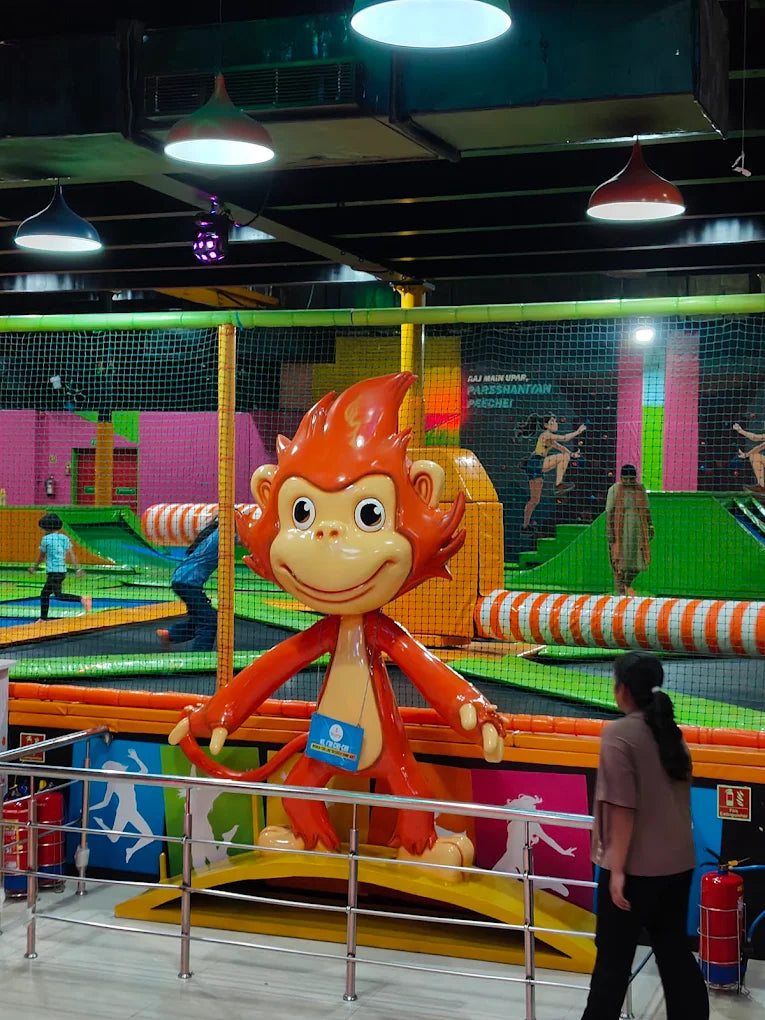 A large monkey statue stands in a trampoline park with children playing in the background. A young person walks past the statue.