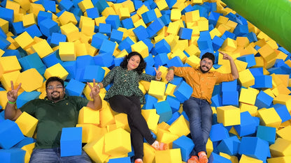 Three young adults pose for a photo in a foam pit filled with blue and yellow cubes.