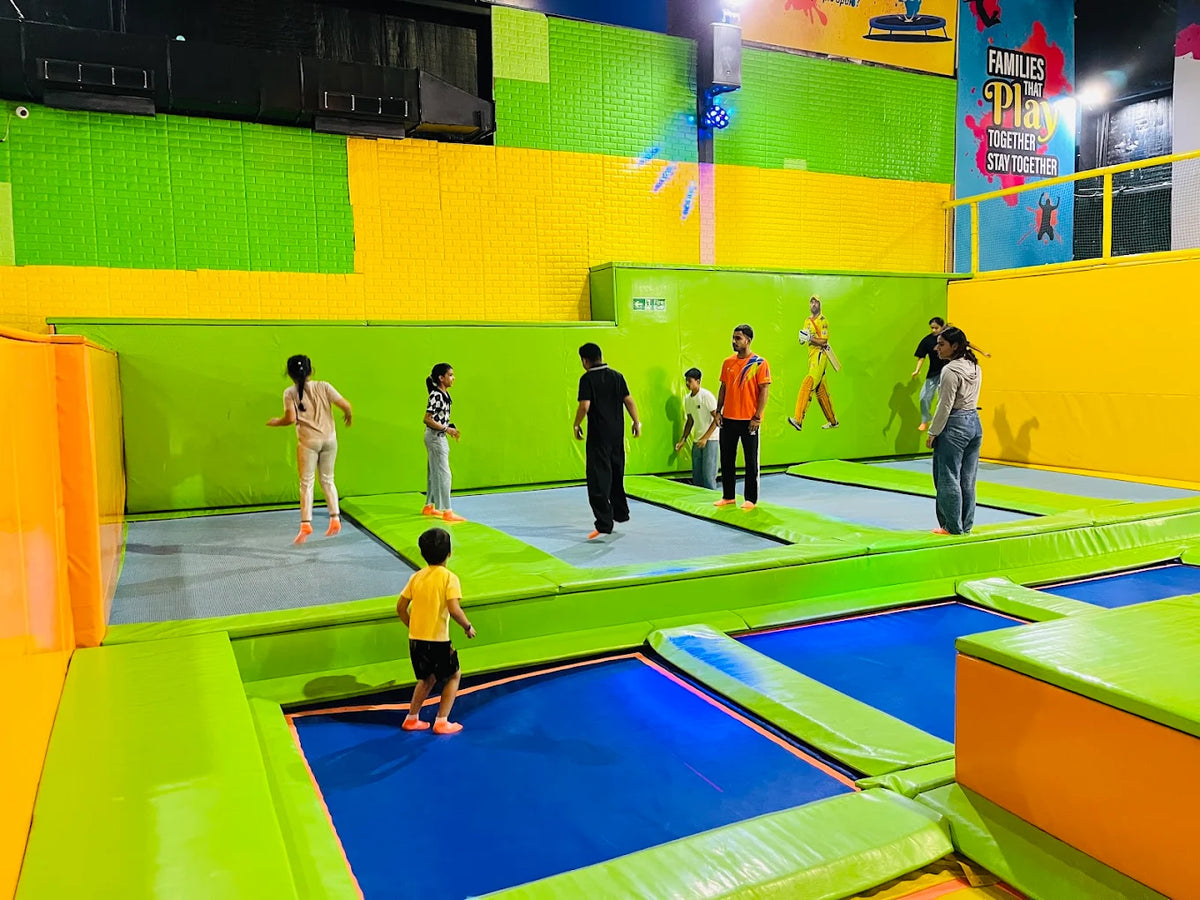Children and adults jump on trampolines in a brightly colored indoor play area.