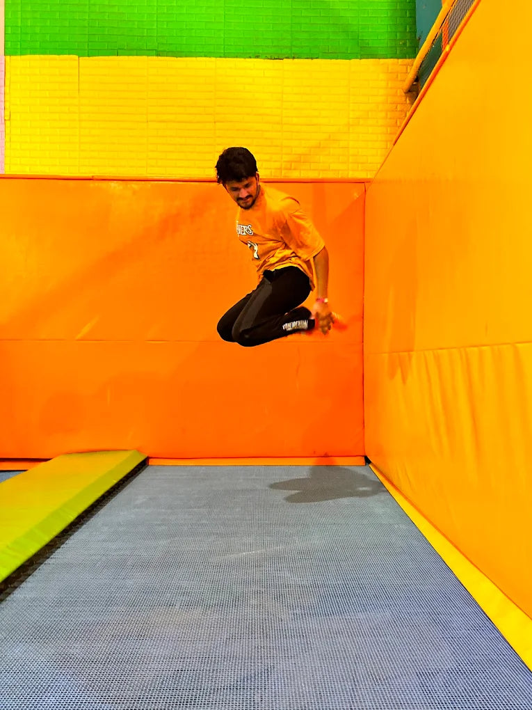A young man in mid-air jumps on a trampoline in a colorful indoor play area.
