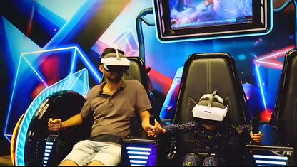 A man and a child in VR headsets sit in futuristic chairs, holding controllers. They are in a brightly lit arcade with neon blue and pink accents.