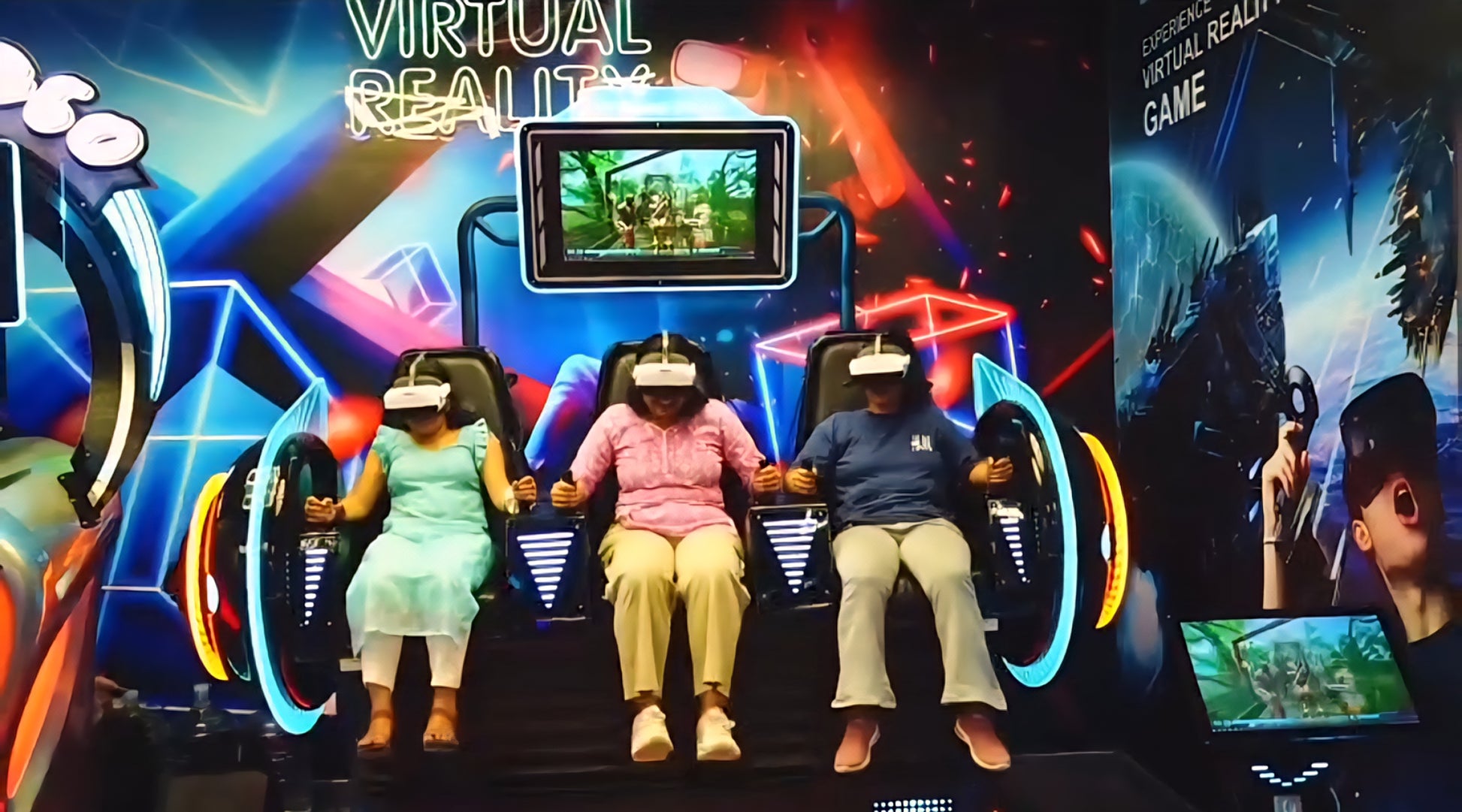 Three young people in VR headsets sit in a virtual reality game simulator. The background features bright neon lights and graphics.
