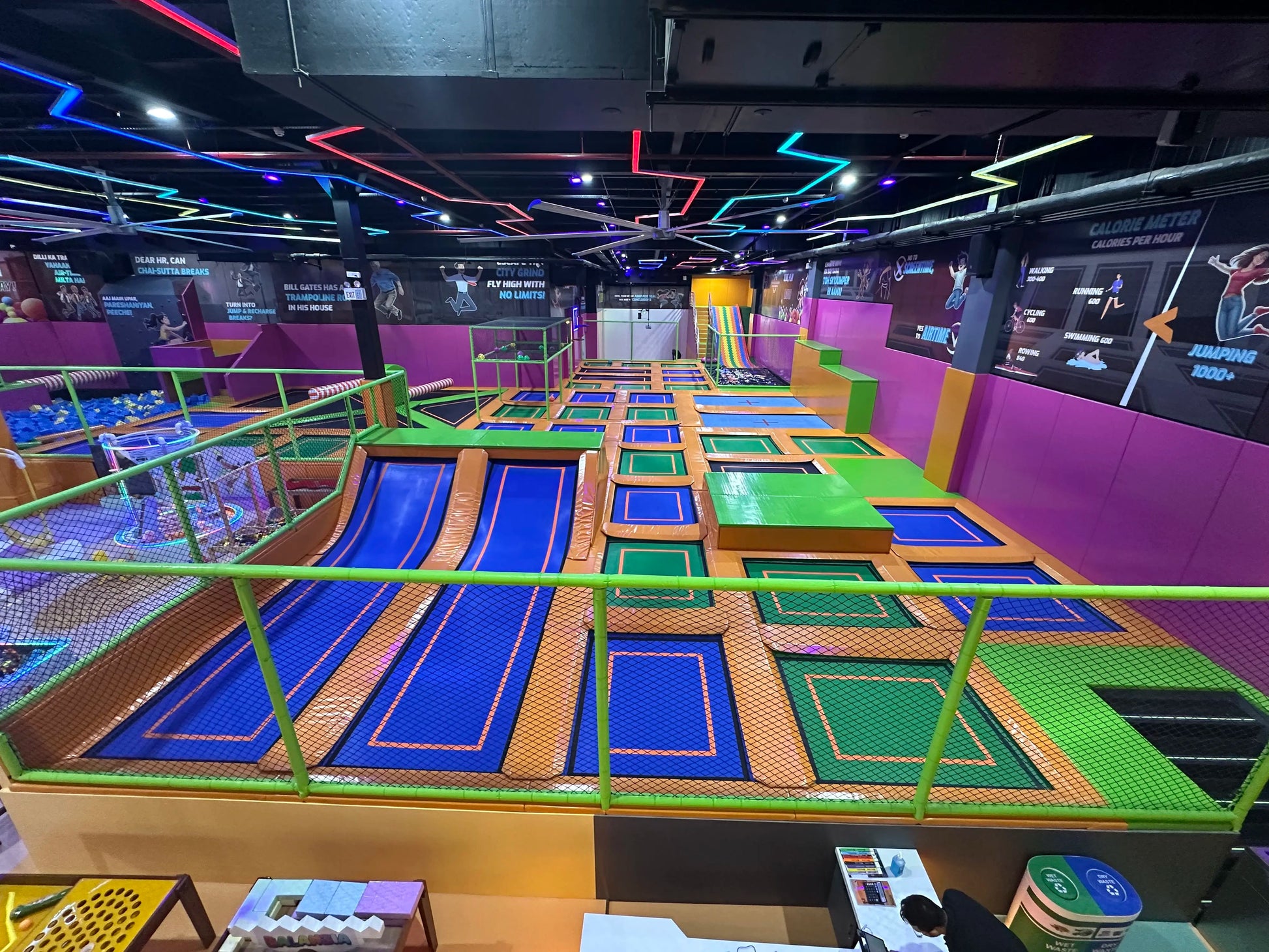 An indoor trampoline park with colorful trampolines and foam pits, featuring a calorie meter display.