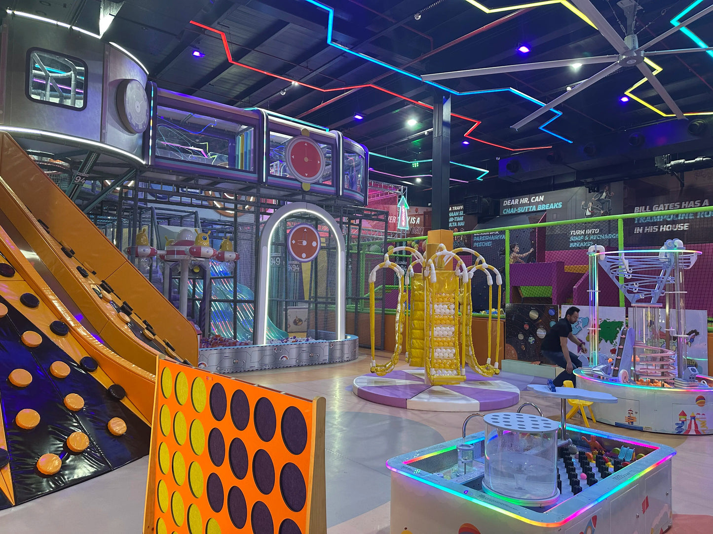 An indoor playground with colorful slides, climbing walls, and interactive games, filled with children.