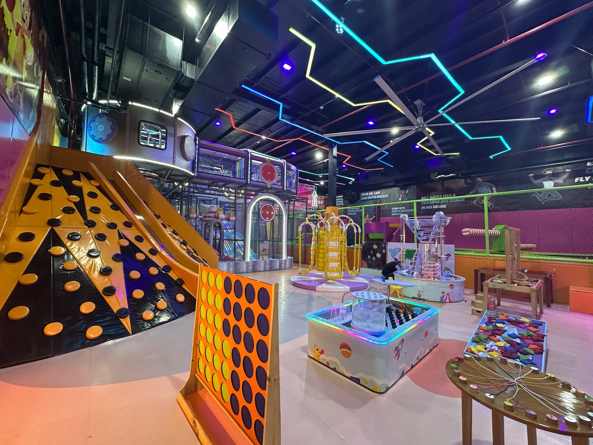 A vibrant indoor play area for children with slides, climbing walls, and interactive games. The space is brightly lit with colorful neon lights and features various play structures.