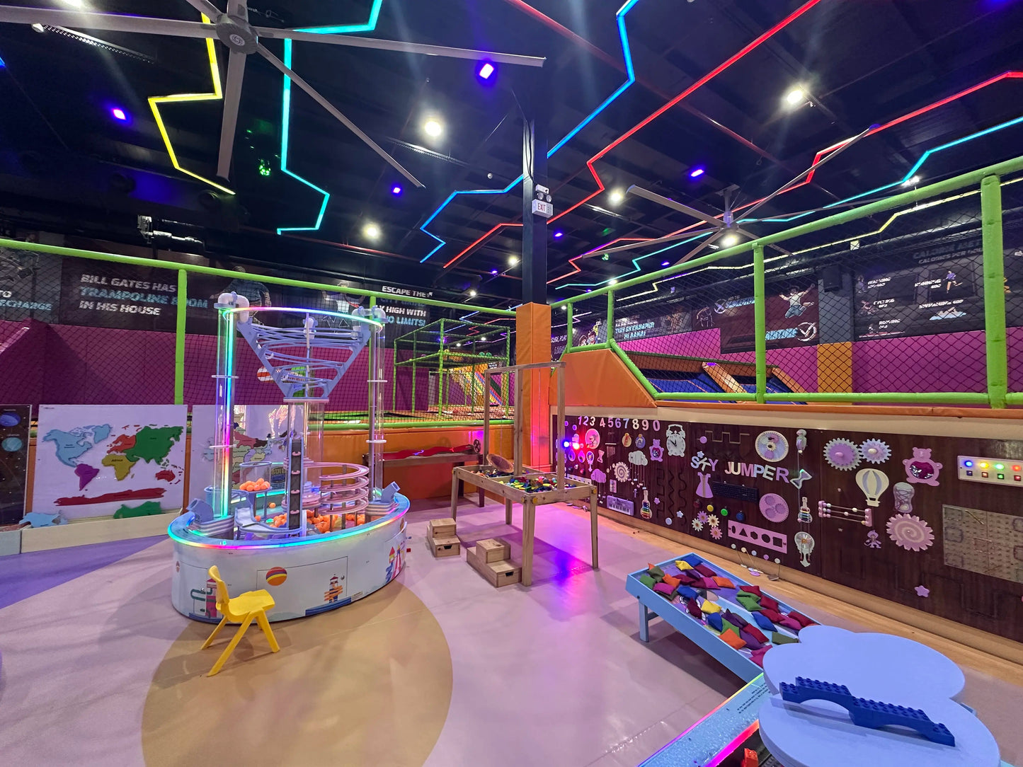 An indoor trampoline park with colorful lights and various play structures for children.