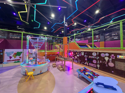 An indoor trampoline park with colorful lights and various play structures for children.