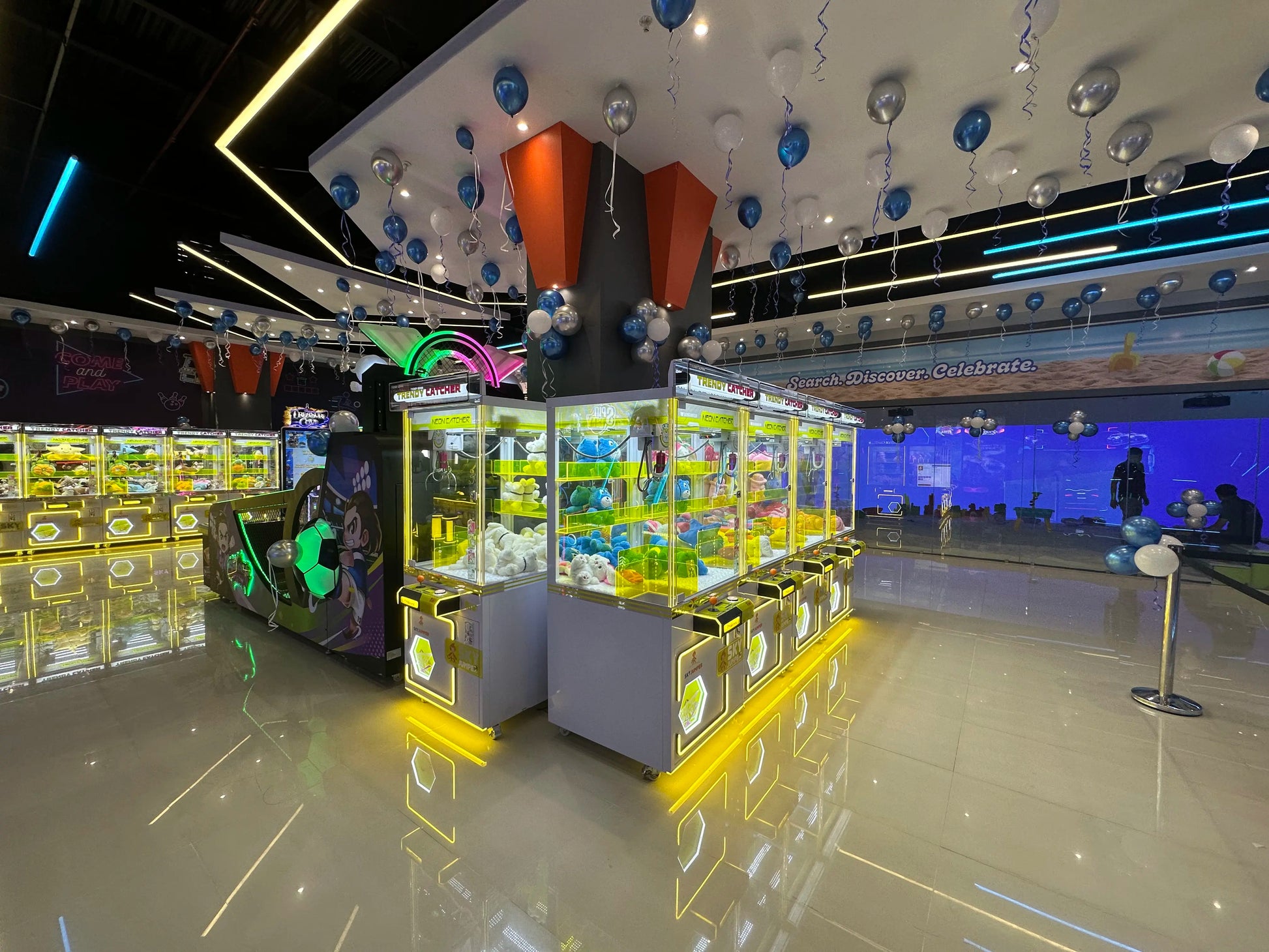 Arcade with claw machines filled with plush toys, decorated with balloons and neon lights.