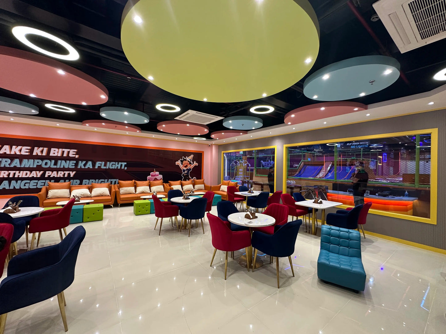 A brightly lit indoor play area with trampolines and a seating area for adults.