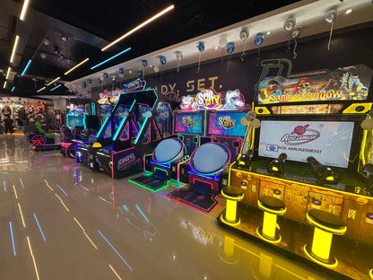 An arcade with colorful lights and game machines, including racing simulators and basketball games.