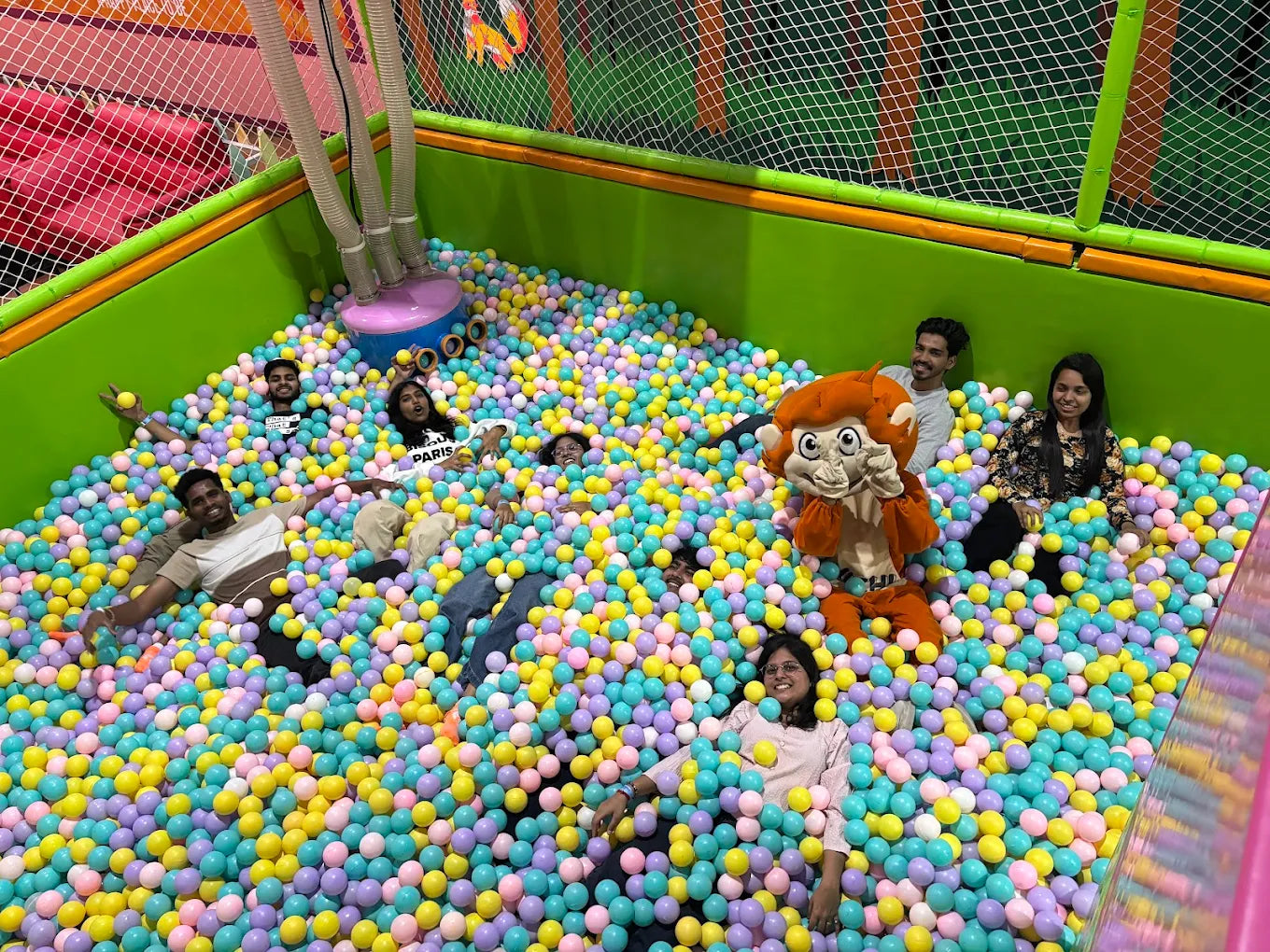 Young adults play in a ball pit with a monkey mascot.