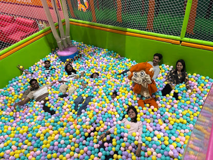 Young adults play in a ball pit with a monkey mascot.
