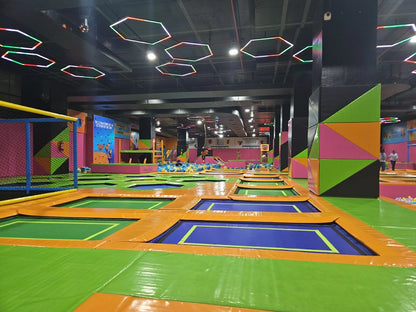 An indoor trampoline park with many trampolines and colorful padding, with a few children jumping.