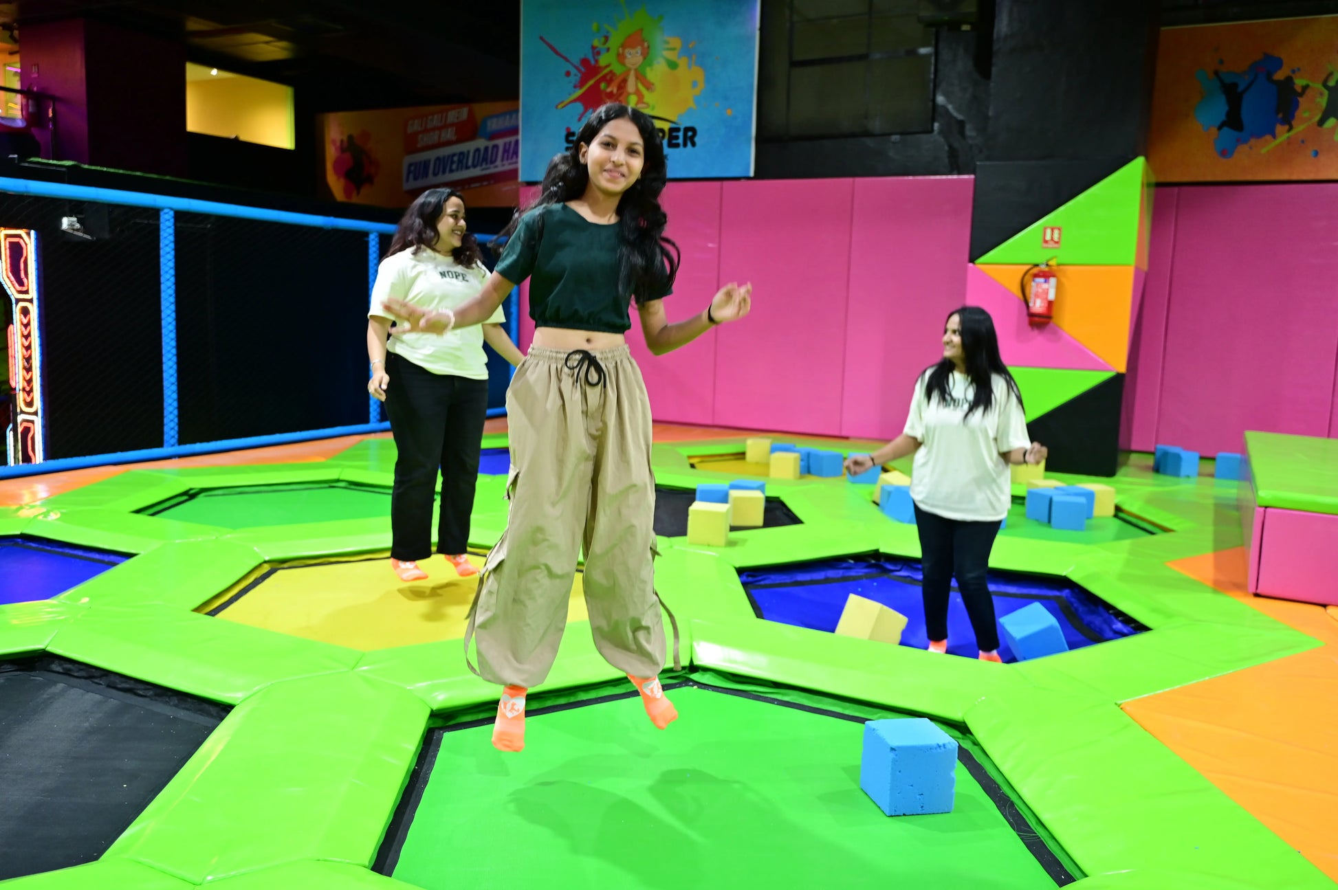 Young women jump on trampolines in a colorful indoor play area.
