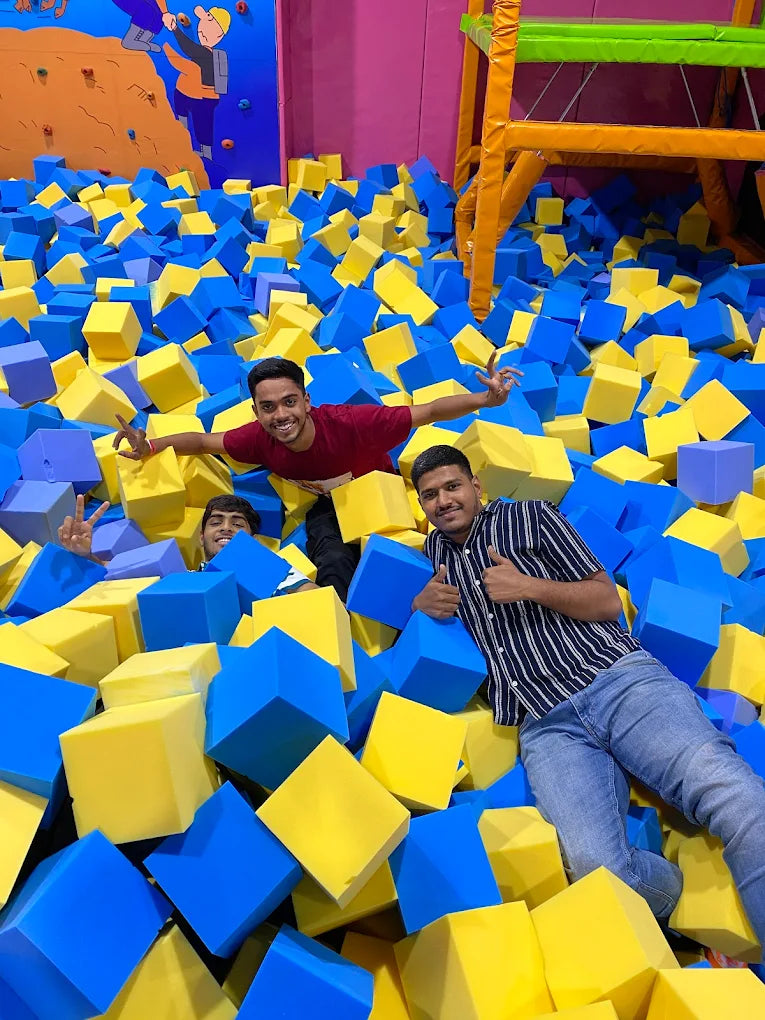 Young adults enjoy a foam pit filled with blue and yellow cubes.