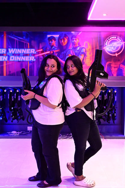 Two young women in laser tag vests hold phasers, ready for action in a neon-lit arena.