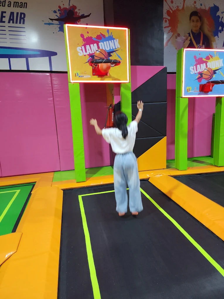 A young person jumps on a trampoline towards a "Slam Dunk" game.