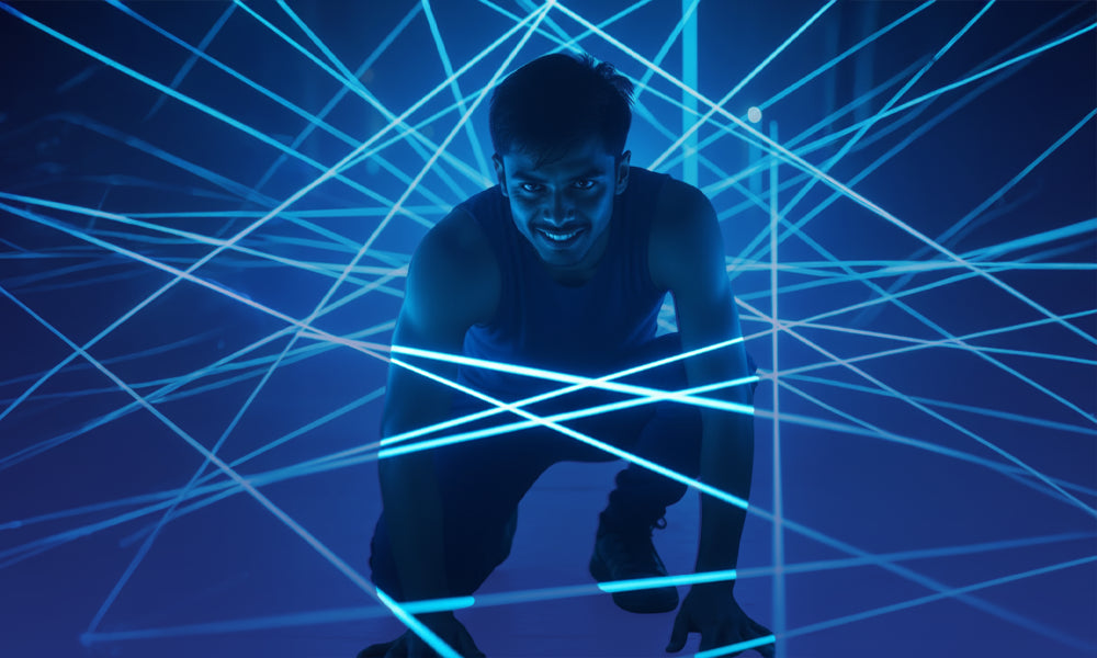 A young man crouches amidst a web of blue laser lights.