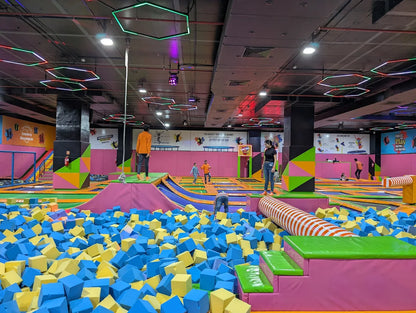 Children and adults enjoy a trampoline park with foam pits and colorful obstacles.