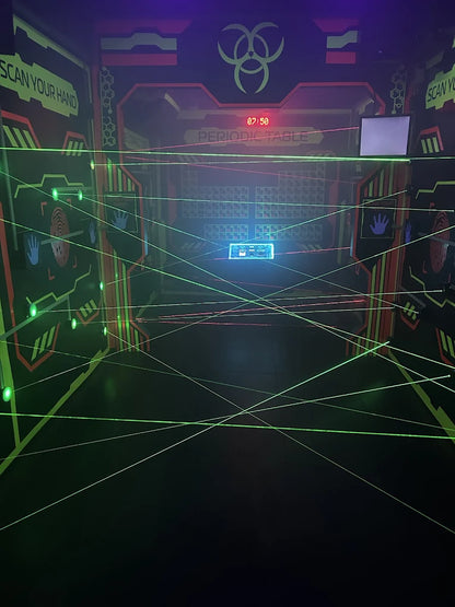 Laser tag arena with a periodic table backdrop and a maze of green lasers.