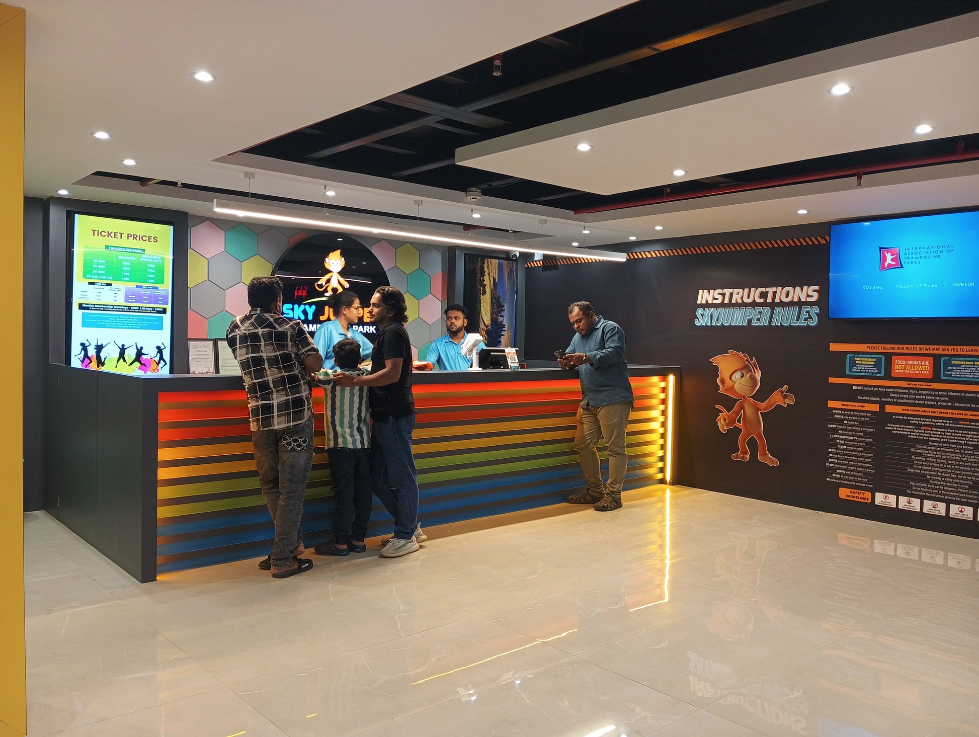 People at a trampoline park's reception desk, with a ticket price display and rules board visible.