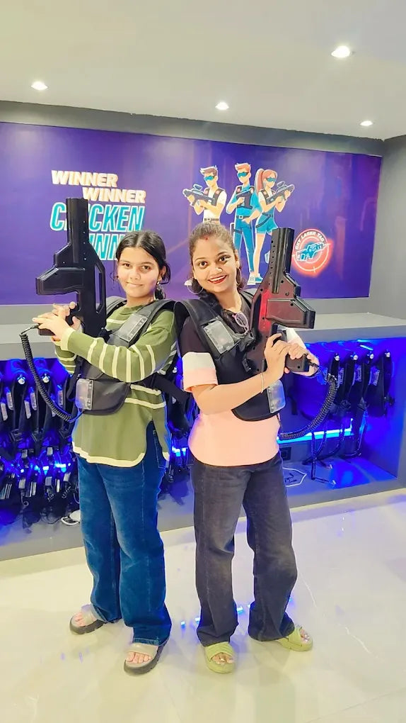 Two young women in laser tag vests and holding phasers smile at the camera in a laser tag arena.
