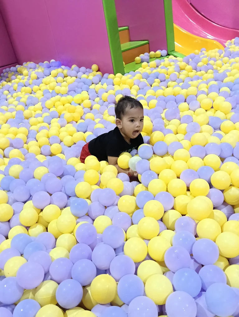 A baby crawls in a ball pit filled with yellow and purple balls.