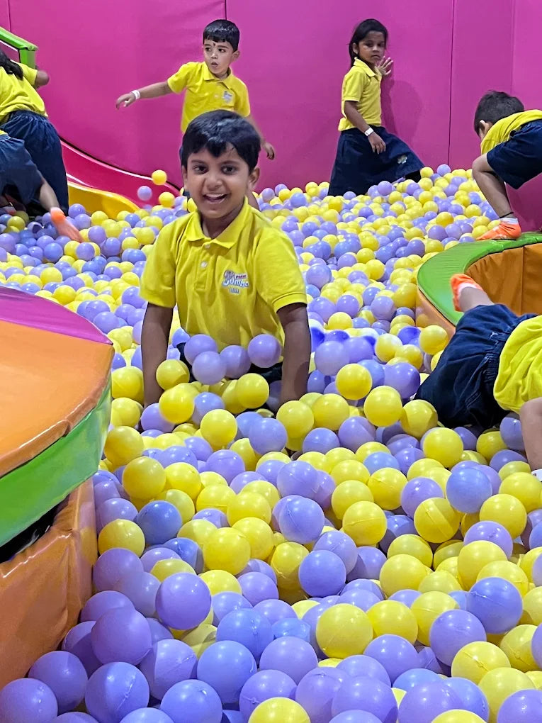 Young children play in a ball pit filled with purple and yellow balls.