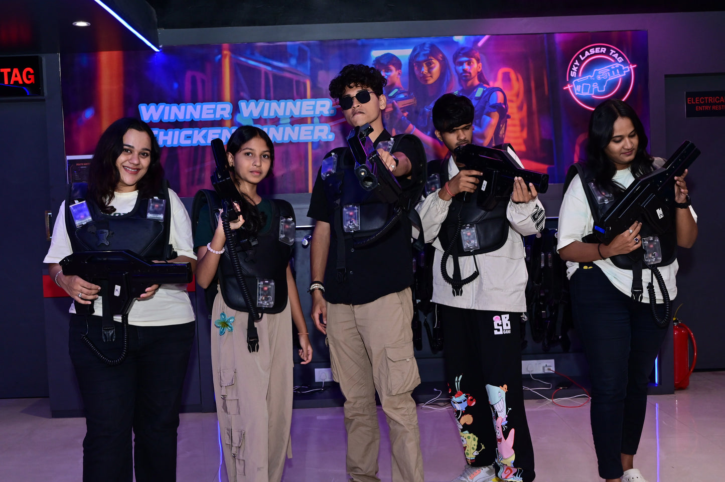 Young adults in laser tag vests and gear pose with their phasers in a neon-lit arena.