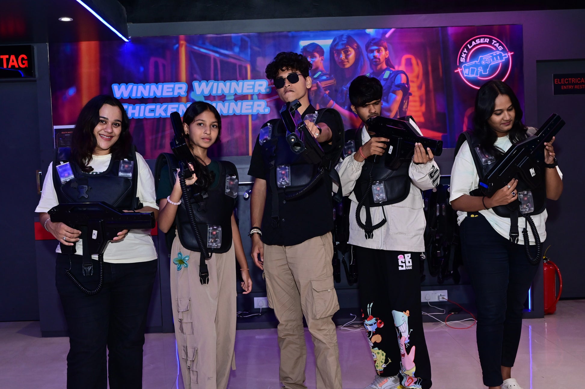 Young adults in laser tag vests and gear pose with their phasers in a neon-lit arena.