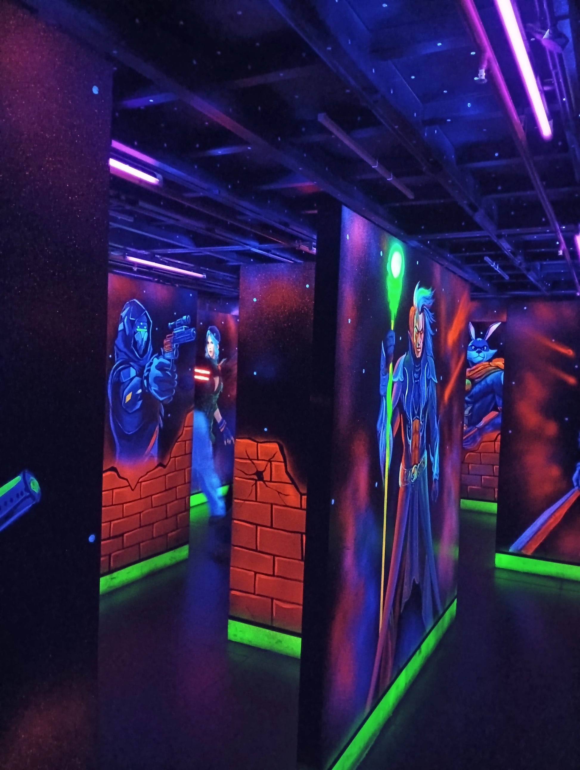 A dimly lit laser tag arena with neon lights and murals of characters.
