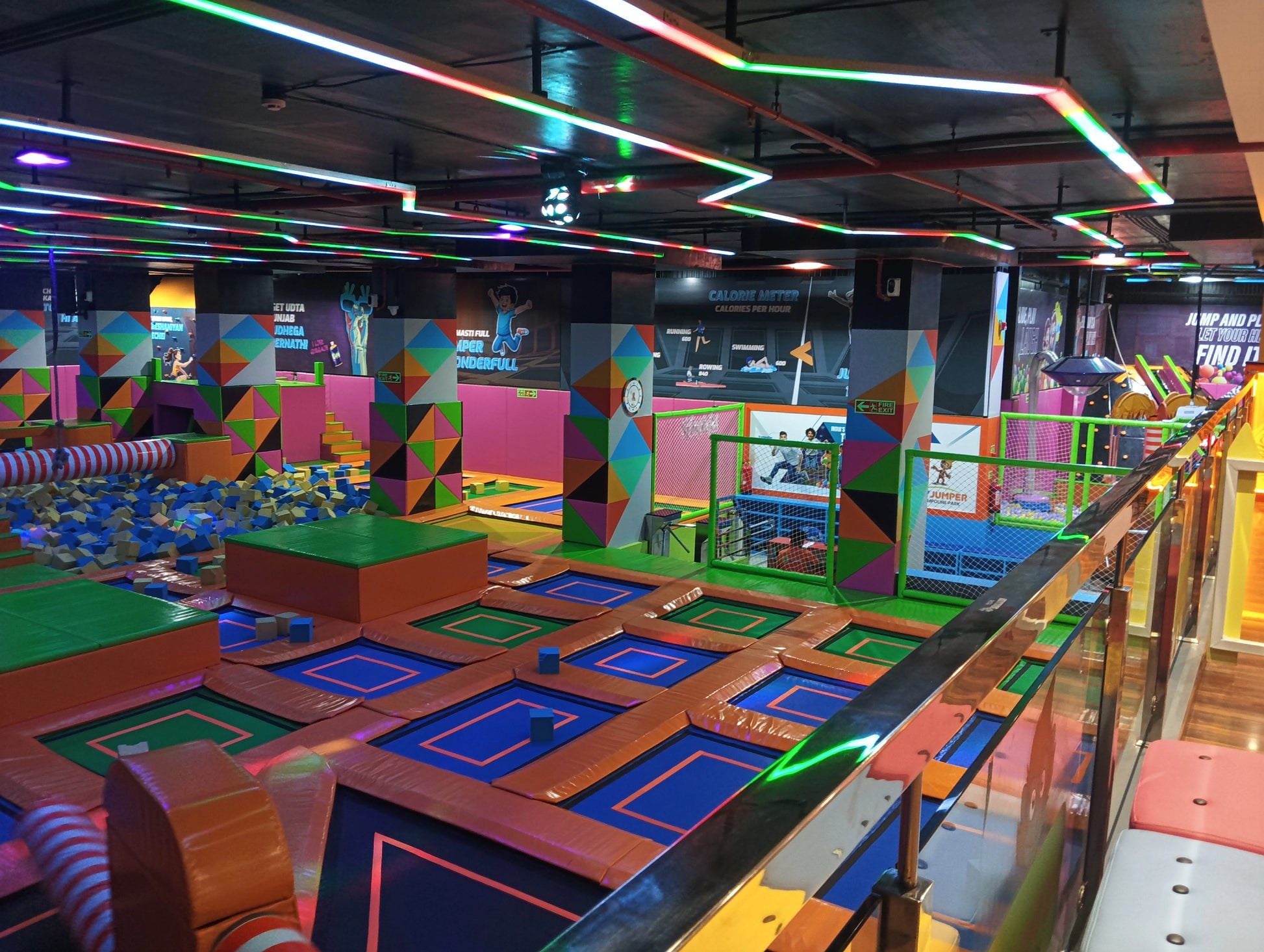 A vibrant indoor trampoline park with colorful foam pits and trampolines, filled with children and young adults.