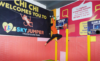 A young person in an orange shirt jumps to dunk a basketball at a trampoline park.