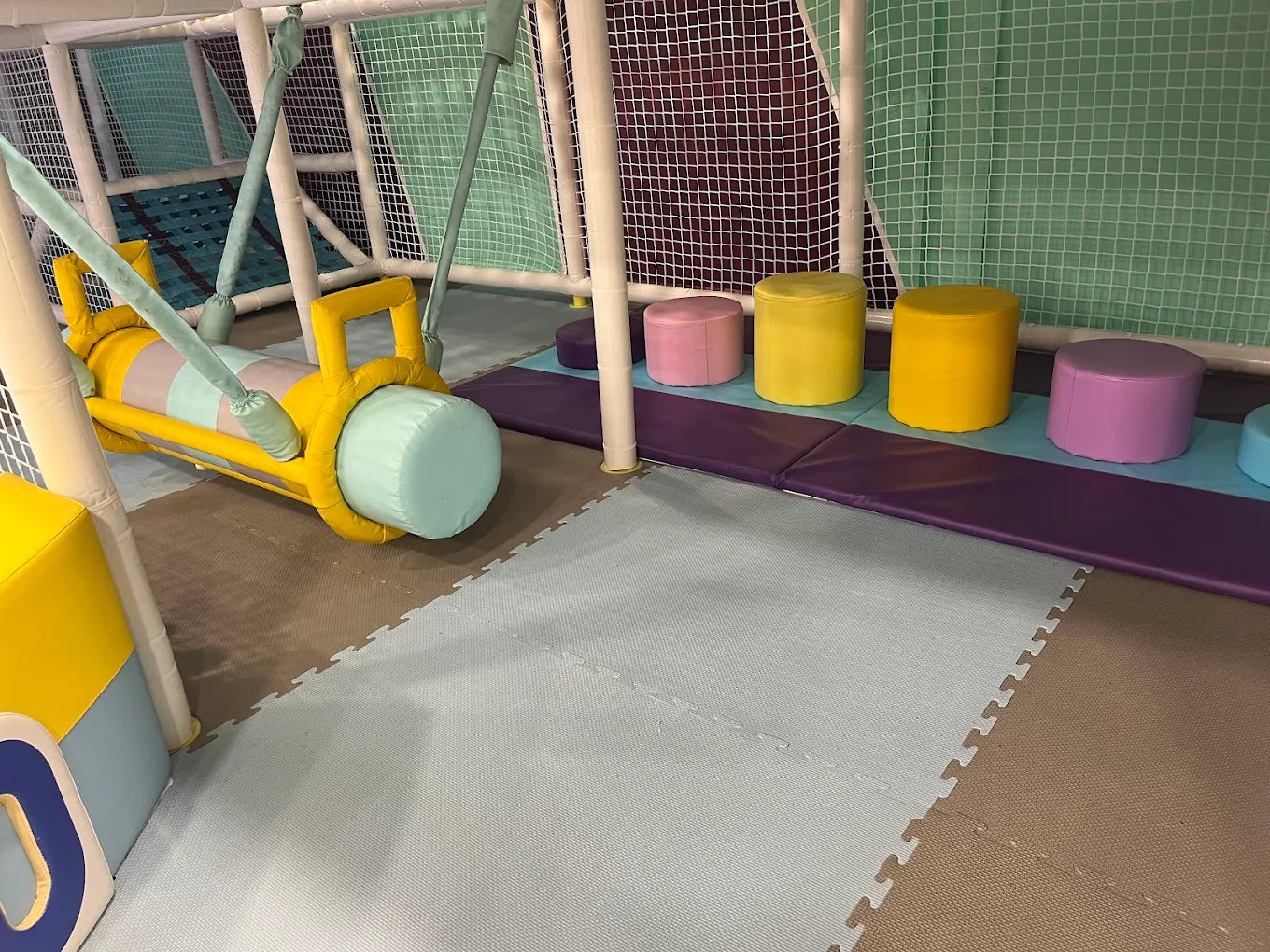 A colorful indoor playground with a soft swing and cushioned seating for children.