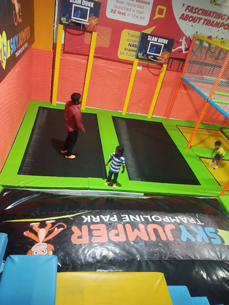 Children and adults enjoy trampolines at an indoor trampoline park with slam dunk hoops.