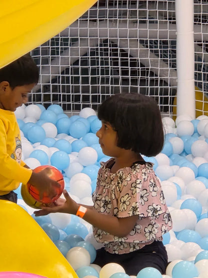 Two young children play with a ball in a ball pit filled with blue and white balls.
