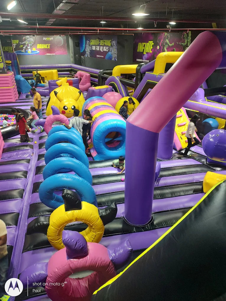 Children play on a large, colorful inflatable obstacle course with slides and tunnels.