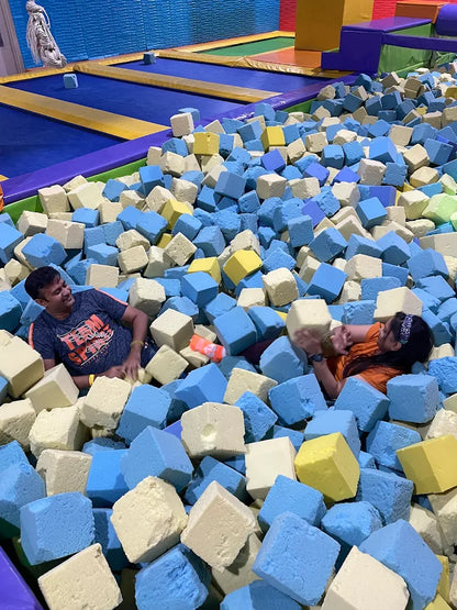 Two adults play in a foam pit at a trampoline park.