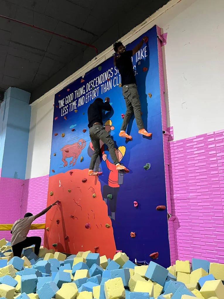 Young adults rock climbing on a colorful wall above a foam pit.
