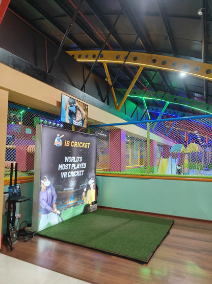 A VR cricket setup with a large banner and a young person playing. The background shows a colorful indoor playground.