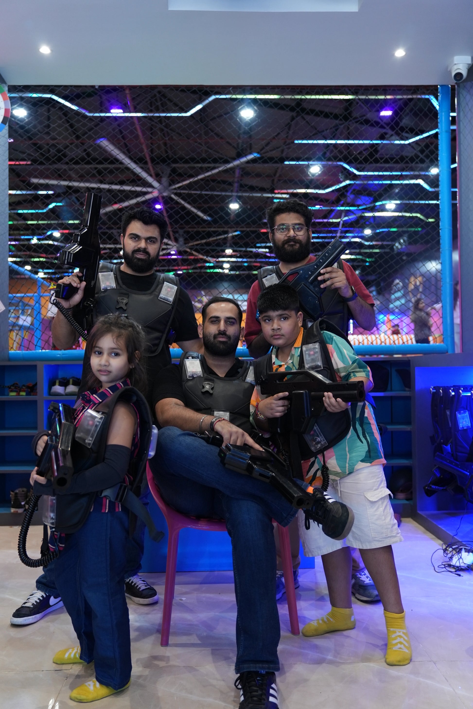 A family poses with laser tag gear and guns in a dimly lit, neon-lit arena.